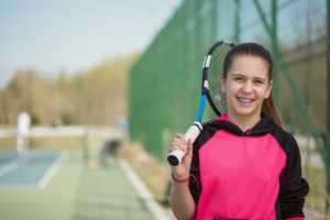 Young Girl With Braces Smiling and Holding A Tennis Racket