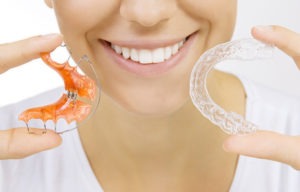 Beautiful smiling girl holding a Hawley and Essix retainer