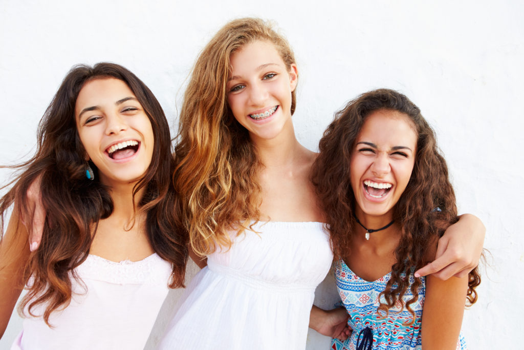 Portrait Of Three Teenage Laughing Girls Leaning Against Wall