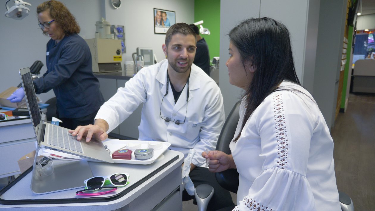 Orthodontist consulting with a patient about treatment options, laptop and orthodontic tools visible, in a modern dental office setting.